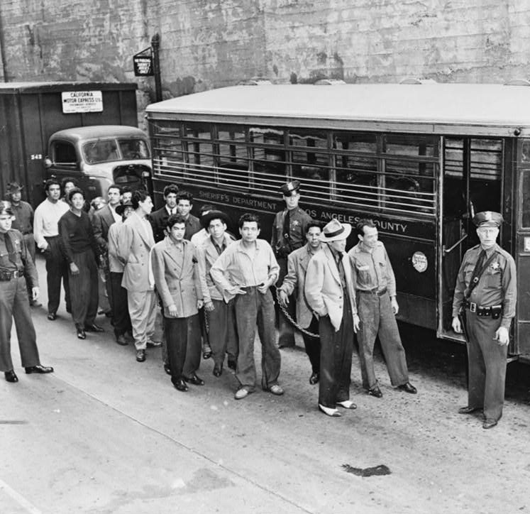 Zoot suiters lined up outside Los Angeles jail en route to court after feud with sailors. Black and white photo.
