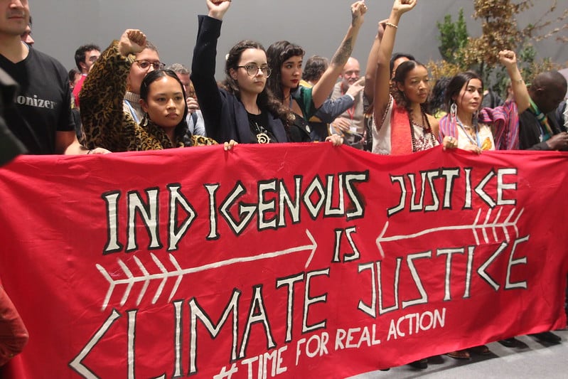 Protestors at the Fridays 4 Future protest inside COP 25 in 2019 holding a sign reading "Indigenous Justice is Climate Justice."